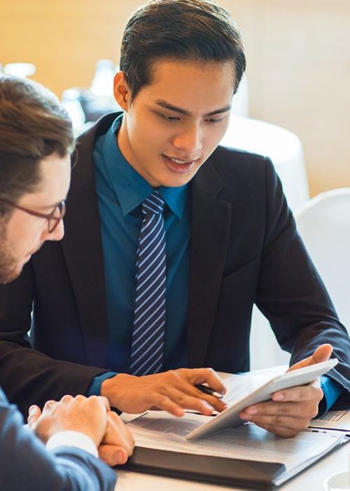 Closeup of two content adult business men sitting at table, using tablet computer, working with documents and discussing them in cafe